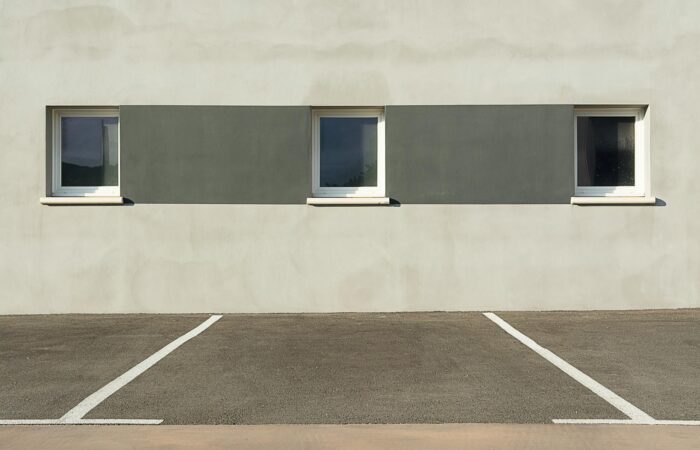 A modern building facade with three windows, featuring a minimalist design and an empty parking lot in the foreground. A modern building facade with three windows, featuring a minimalist design and an empty parking lot in the foreground.