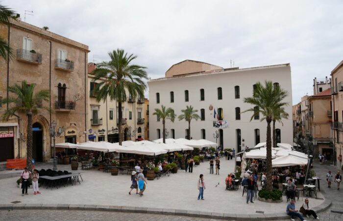 Busy Piazza Del Duomo in Cefalù, Italy, bustling with people and cafes under a cloudy sky. Busy Piazza Del Duomo in Cefalù, Italy, bustling with people and cafes under a cloudy sky.