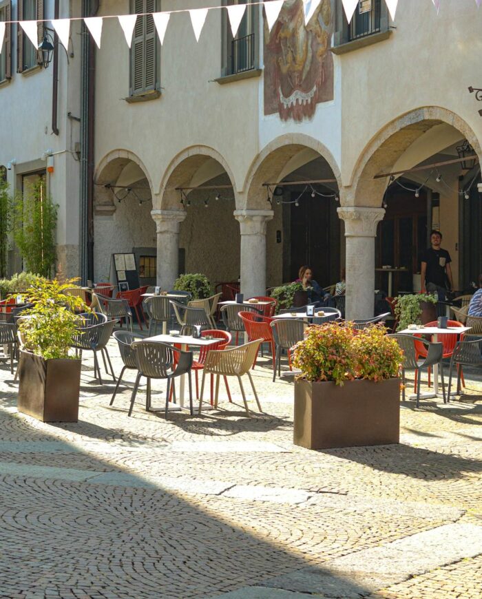 A picturesque outdoor café with vibrant seating and plants in a sunlit European piazza.