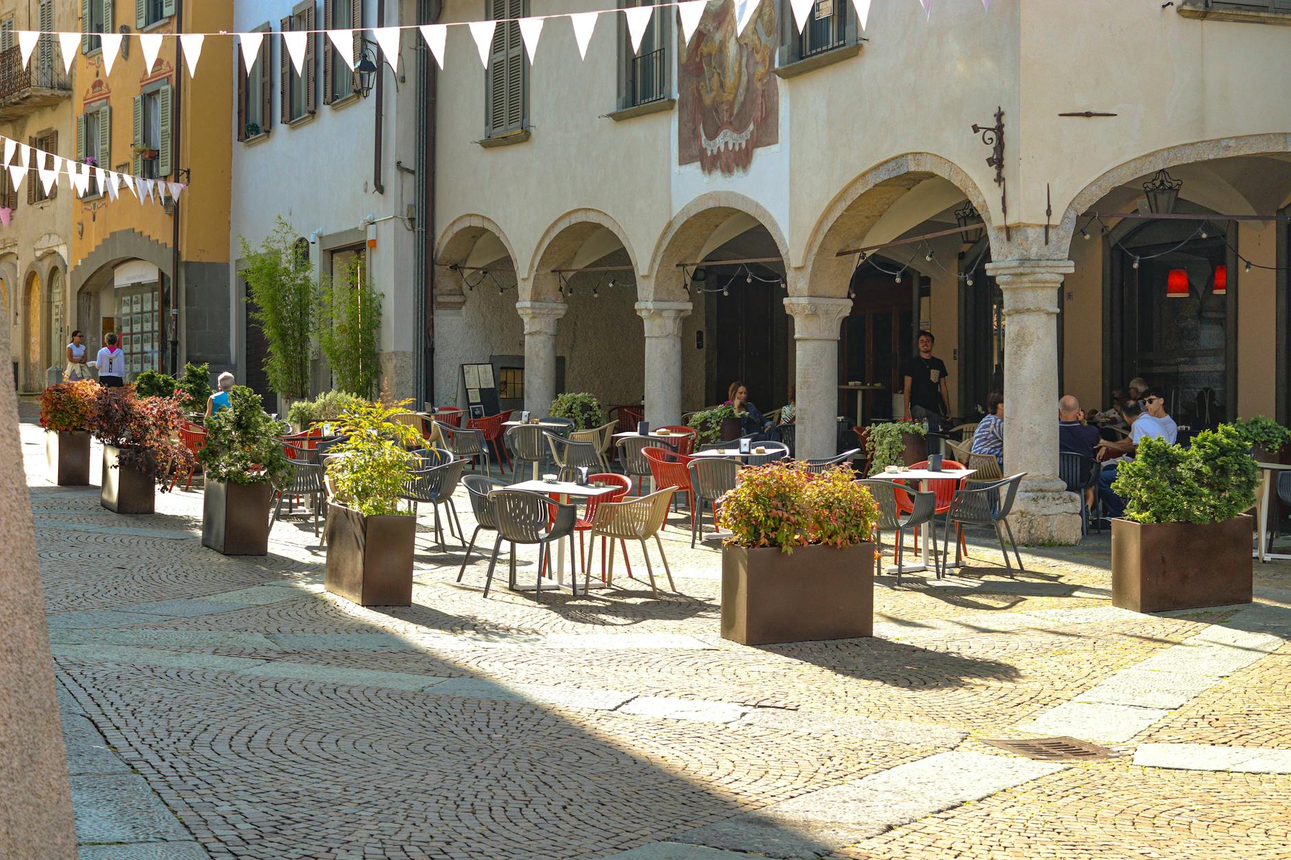 A picturesque outdoor café with vibrant seating and plants in a sunlit European piazza.