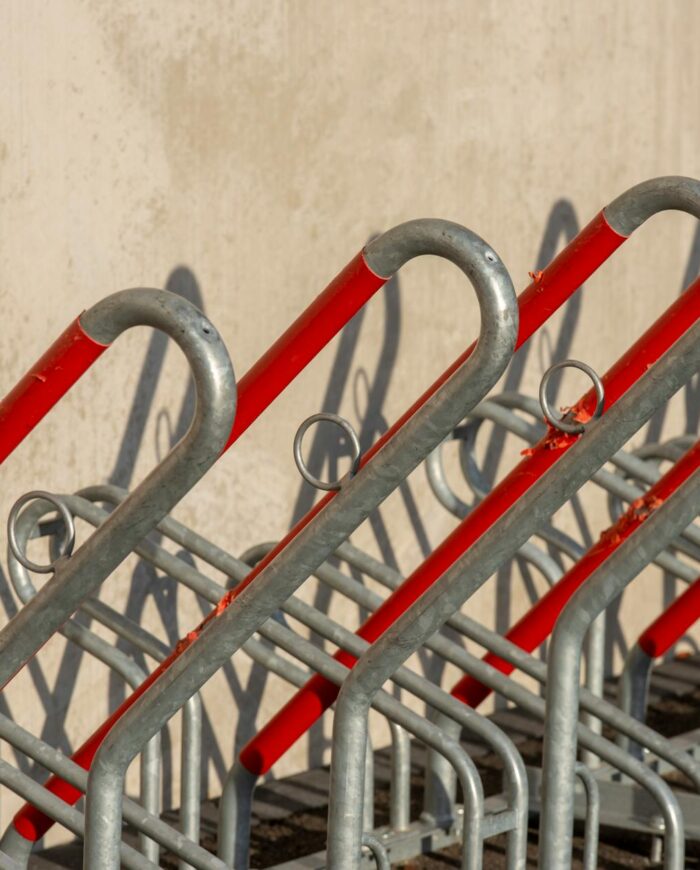 Empty bicycle rack with red and silver metal bars creating a geometric pattern in outdoor setting.