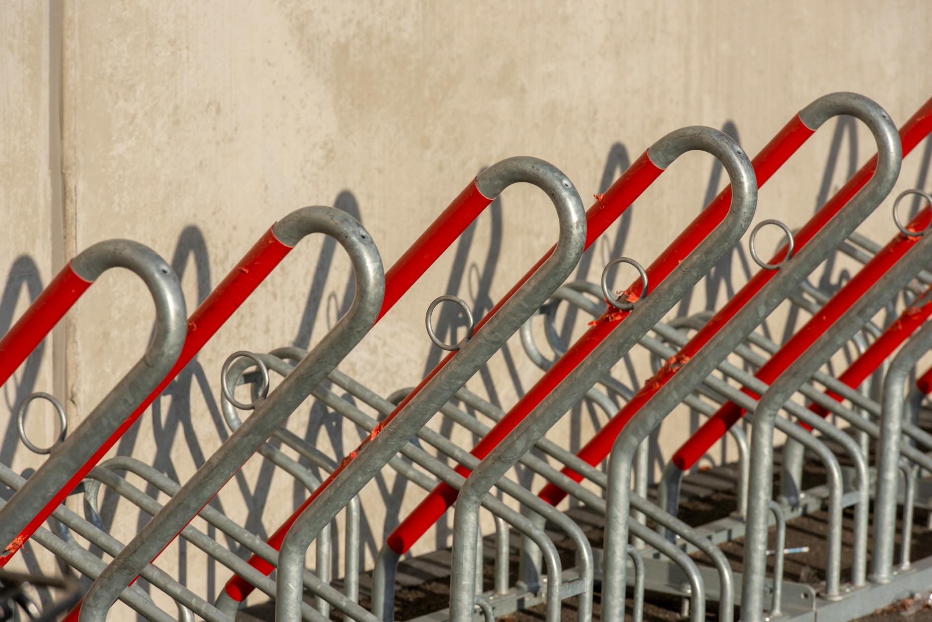 Empty bicycle rack with red and silver metal bars creating a geometric pattern in outdoor setting.