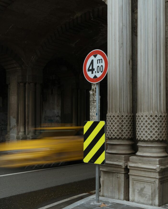 A yellow taxi speeds through a stone tunnel with classic columns and arches, creating a blur of motion.