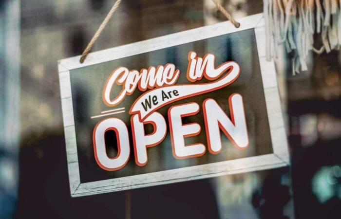 A welcoming ‘Come in, We Are Open’ sign hanging on a glass window of an urban shop. A welcoming 'Come in, We Are Open' sign hanging on a glass window of an urban shop.