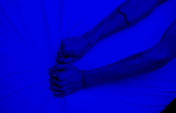Close-up of tattooed arms pulling fabric under intense blue lighting, symbolizing stress or frustration.
