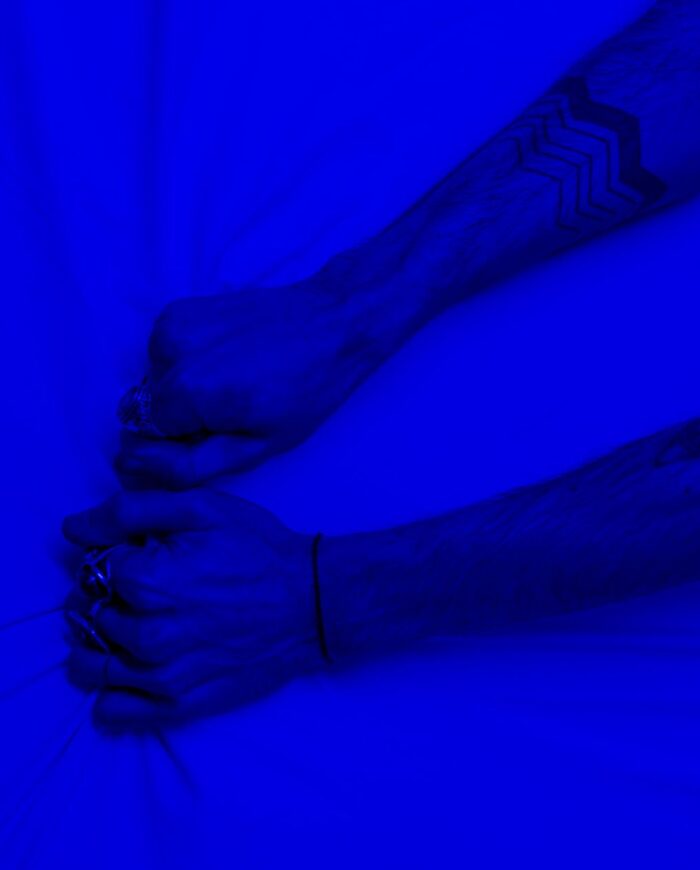 Close-up of tattooed arms pulling fabric under intense blue lighting, symbolizing stress or frustration.