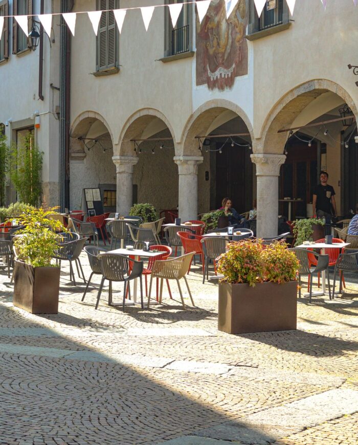 A picturesque outdoor café with vibrant seating and plants in a sunlit European piazza.