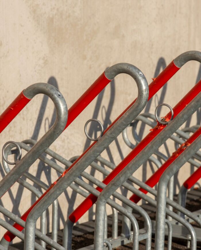 Empty bicycle rack with red and silver metal bars creating a geometric pattern in outdoor setting.