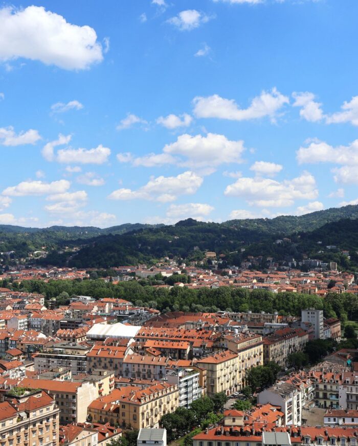 Stunning aerial view of Turin, Italy with red rooftops and lush green hills under a clear blue sky.