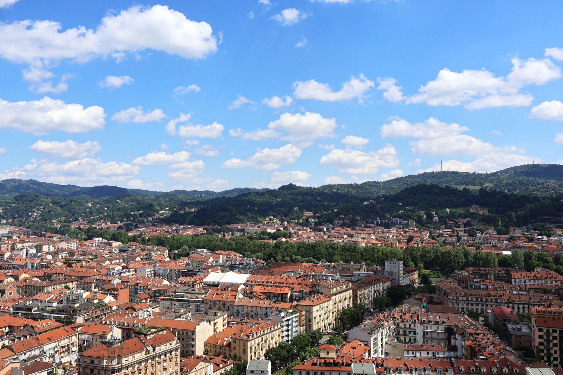 Stunning aerial view of Turin, Italy with red rooftops and lush green hills under a clear blue sky.