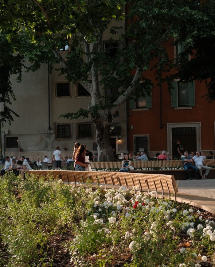 People relax on benches surrounded by flowers in Verona's charming architecture.