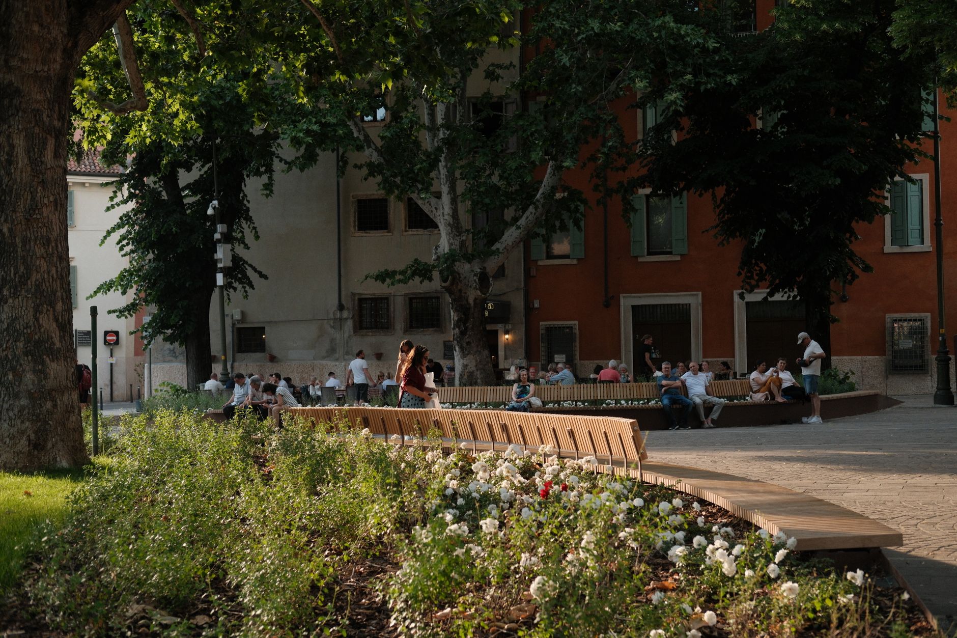 People relax on benches surrounded by flowers in Verona's charming architecture.
