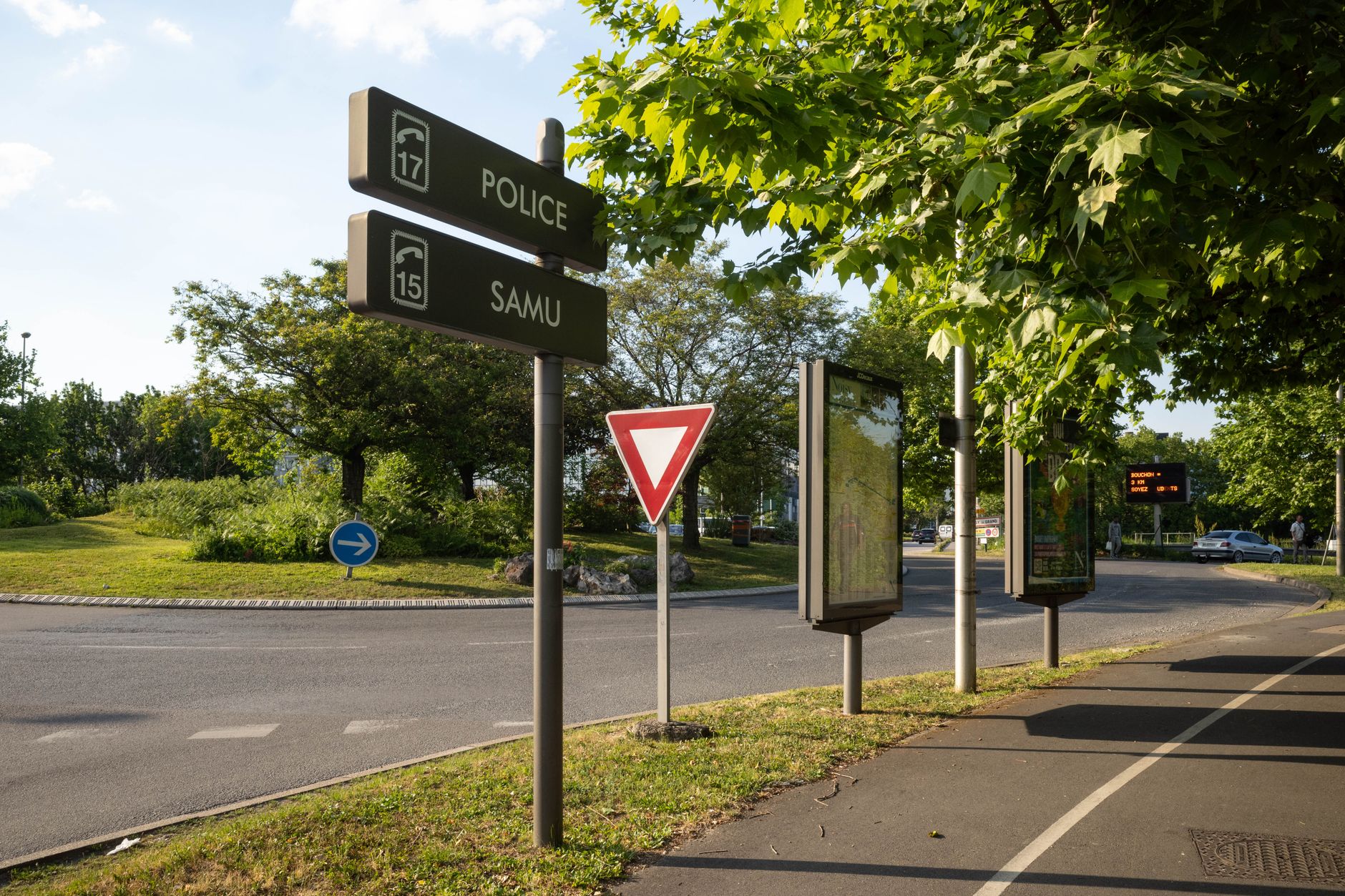 Roundabout in France with traffic signs and lush greenery on a sunny day.